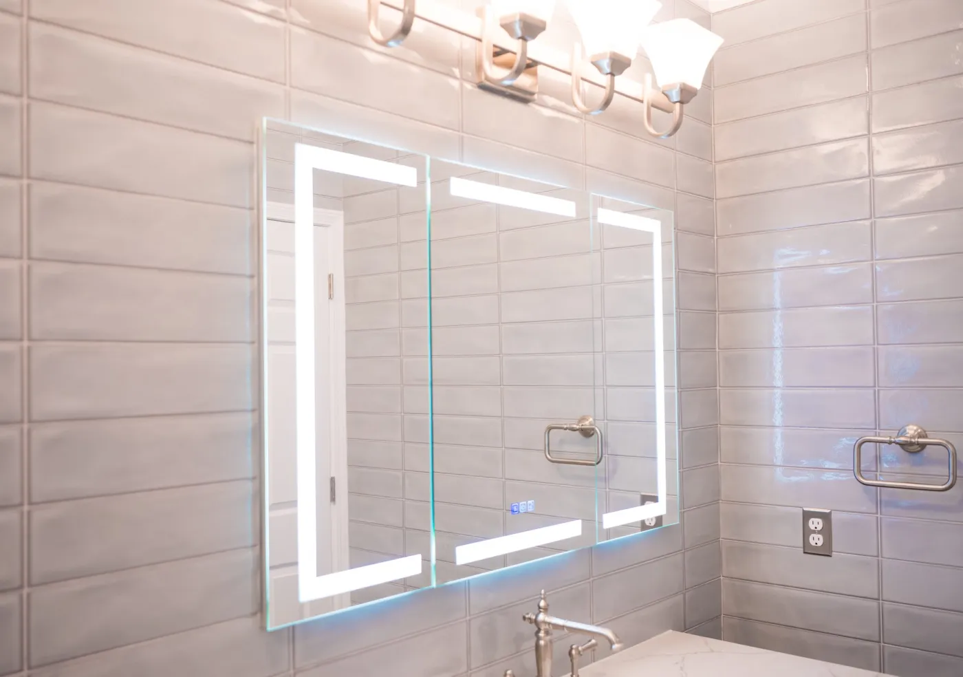 Backlit LED mirror against floor-to-ceiling gray tile in a remodeled Ypsilanti bathroom