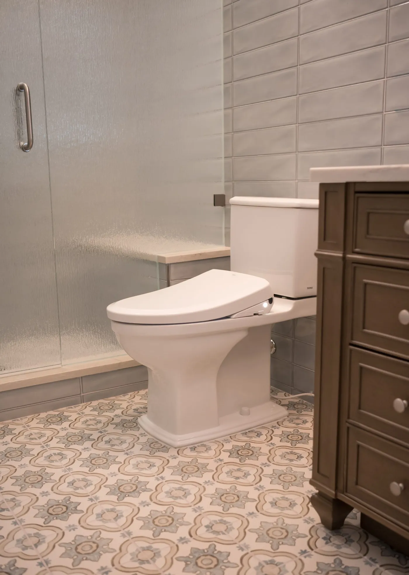 Comfort height toilet beside the shower bench and patterned floor tile